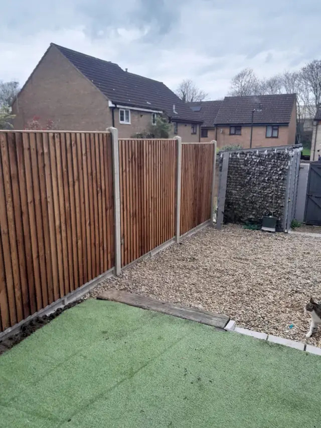 New feather-edge fence panels on concrete posts beside artificial grass and a gravel area
