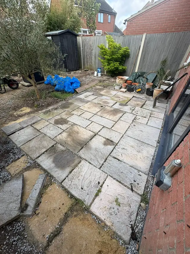 Back garden before work, with broken old paving and bare ground around an olive tree