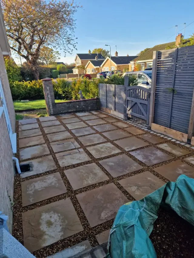 Paving slabs with gravel joints laid by Asbe-bloom beside a grey slatted fence and gate